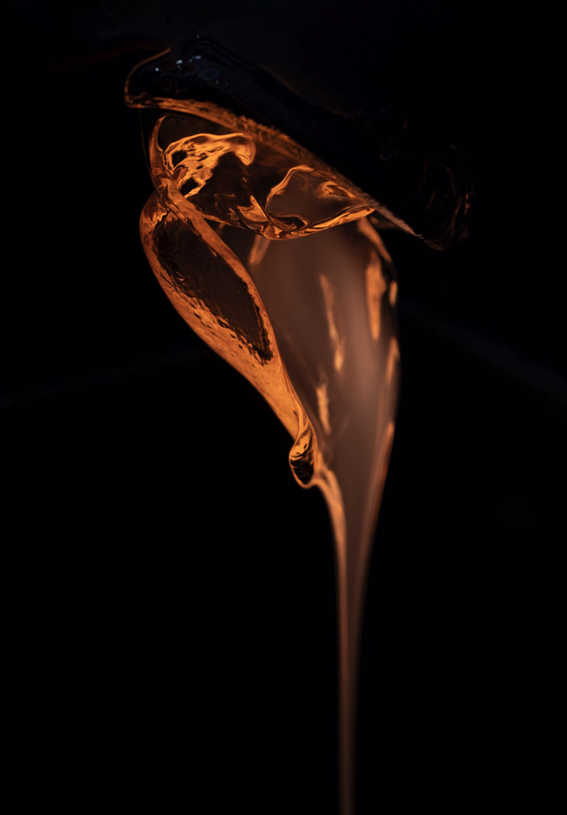 viscous fluid pouring in warm light against black background